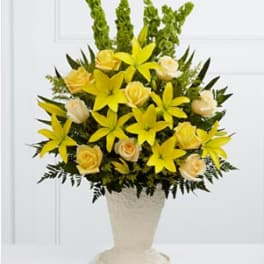 Yellow lilies and pale roses arranged in a cream pedestal vase