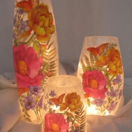 Three lit floral-patterned glass candle holders with butterflies