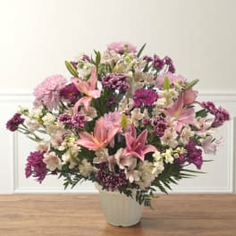 Pink lilies and purple mixed flowers arranged in a white vase