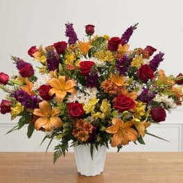 Mixed bouquet of red roses, orange lilies, and purple flowers in a white vase