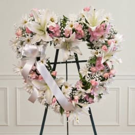 Heart-shaped floral wreath with white lilies and pink flowers on a stand