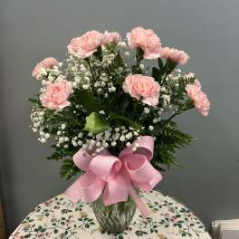 Pink carnations and baby's breath in a glass vase with a pink bow