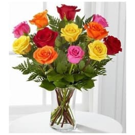 Arrangement of mixed-color roses in a clear glass vase on a white table.