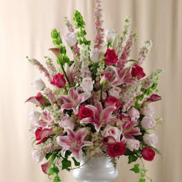 Tall pink and white floral arrangement with lilies and roses in a white pedestal vase