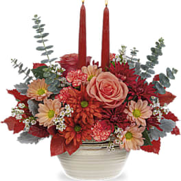 Red and peach floral arrangement with two red taper candles in a white bowl