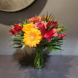 Mixed bouquet of bright gerbera daisies, lilies, and alstroemeria in a glass vase