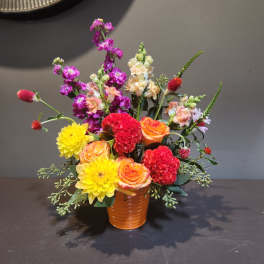 Mixed bouquet in an orange vase with yellow, orange, red, and purple blooms