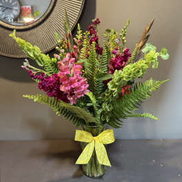 Mixed pink and magenta flowers in a glass vase with a yellow ribbon