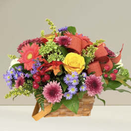 Mixed bouquet in a woven basket with a red ribbon and bright flowers