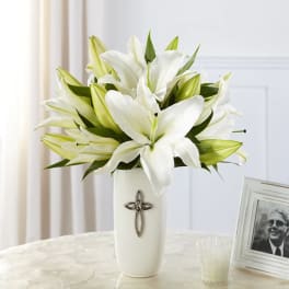 White lilies arranged in a white vase with a cross emblem