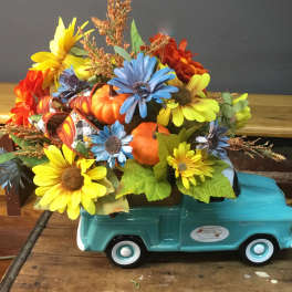 Fall floral arrangement in a turquoise truck-shaped container with pumpkins