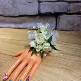 White rose wrist corsage on a mannequin hand with sheer ribbon