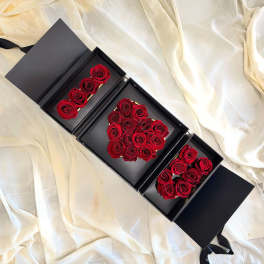 Black gift boxes with red roses arranged inside on cream fabric