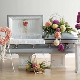 Casket surrounded by pastel floral arrangements and a heart-shaped wreath