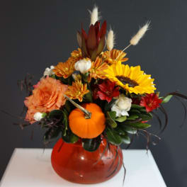 Autumn floral arrangement with a small pumpkin in a red glass vase