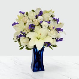 White lilies and roses in a blue glass vase with purple accents