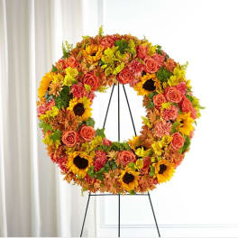 Circular floral wreath on a black stand with sunflowers and roses