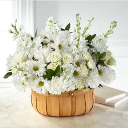 White floral arrangement in a wooden basket with daisies and roses