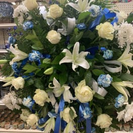 Standing floral spray with white lilies, cream roses, and blue ribbons