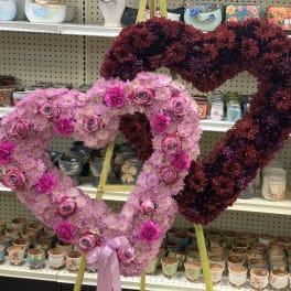 Two heart-shaped floral arrangements on stands, one pink and one burgundy.