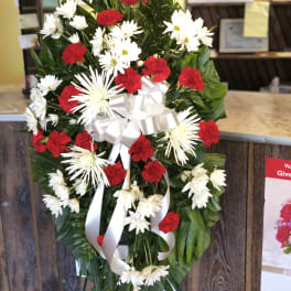 Standing floral wreath with red carnations and white daisies, tied with a white ribbon