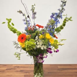 Tall mixed bouquet in a glass vase with orange, yellow, blue, and purple flowers