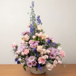 Pastel floral arrangement in a woven basket with tall blue blooms and pink flowers