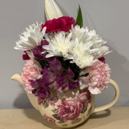 Mixed bouquet of white, pink, and purple flowers in a cream teapot vase