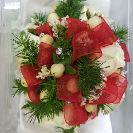Small white floral arrangement with red ribbon and berries in a clear plastic box