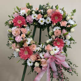 Heart-shaped floral wreath on a stand with pink and white flowers and a pink ribbon