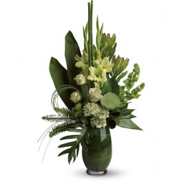 Tall modern arrangement of green and white flowers with large tropical leaves in a green glass vase