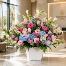 Large mixed flower arrangement in a white vase with pink, blue, and white blooms