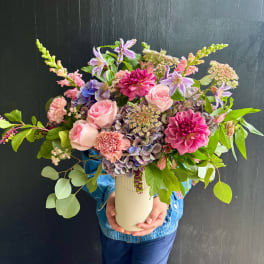 Mixed bouquet of pink, purple, and peach flowers in a cream vase