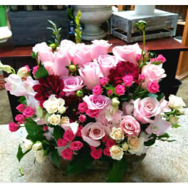 Pink and white rose arrangement with burgundy blooms in a low container