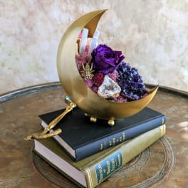 Gold crescent sculpture with a purple rose and crystals on stacked books