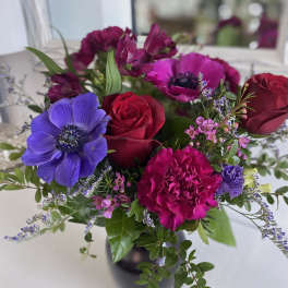Vase arrangement of red roses, magenta carnations, and purple anemones with small pink blooms