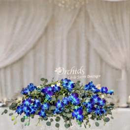 Low floral arrangement with vivid blue orchids and greenery on a wedding table