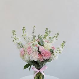 Pink and white bouquet in a clear glass vase with a pink ribbon