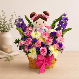 Basket arrangement with a doll surrounded by pink, purple, and white flowers