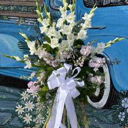Tall white floral standing spray with a white ribbon on an easel