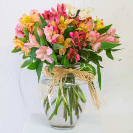 Mixed pink and yellow flowers in a glass vase with a butterfly pick