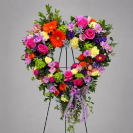 Heart-shaped floral wreath on a stand with bright mixed flowers and a purple ribbon