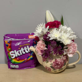 Mixed bouquet in a floral teapot vase beside a purple Skittles bag