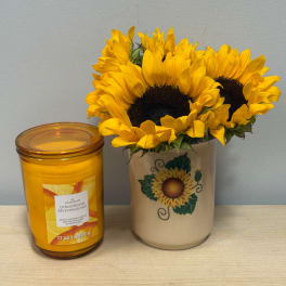 Sunflowers in a ceramic vase beside a yellow candle