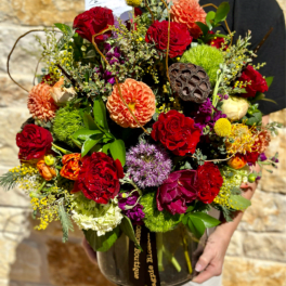 Large mixed bouquet in a glass vase with red, orange, and purple blooms