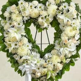Heart-shaped standing wreath of white flowers with a white ribbon bow