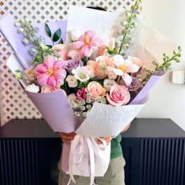 Handheld bouquet of pink and white flowers wrapped in lavender paper