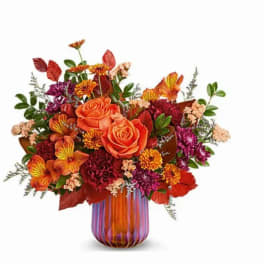 Orange roses and mixed autumn flowers in a striped glass vase