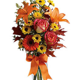 Orange lilies and pink roses in a clear glass vase with an orange ribbon