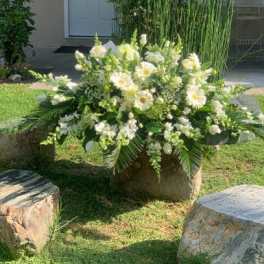 Large white floral arrangement in a stone container outdoors